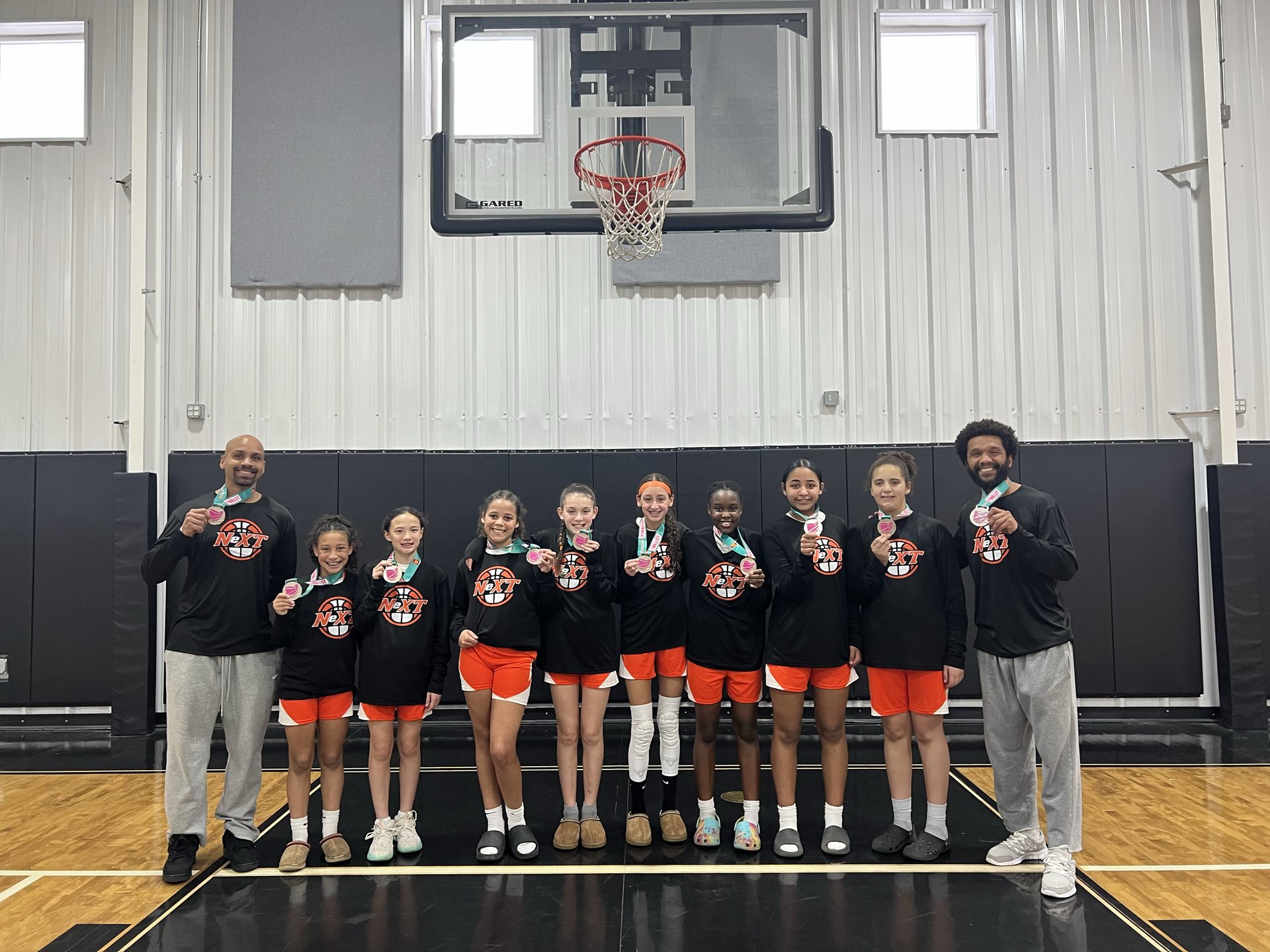 Youth basketball team in orange and black uniforms holding up gold medals